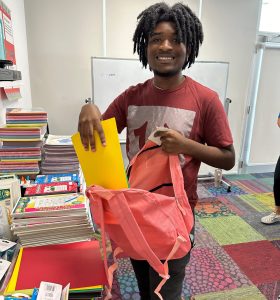 Smiling person packing books into a backpack in a colorful room.